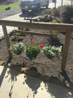 a wooden bench with flowers on it in front of a car parked next to the road