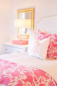 a bed with pink and white pillows on top of it next to a mirror in a room