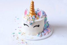 a white cake with a gold horn and unicorn ears on it's head, surrounded by confetti sprinkles