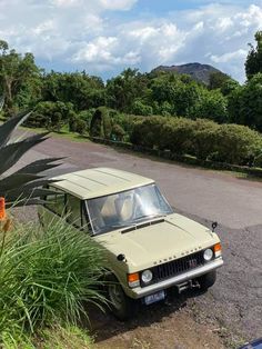 an old car is parked on the side of the road in front of some bushes