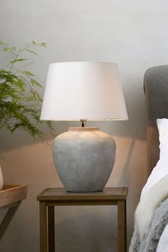 a white lamp sitting on top of a wooden table next to a bed with pillows