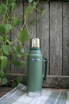 a green insulated thermos sitting on top of a towel next to a potted plant