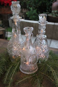 three glass decanters sitting on top of a table next to each other with lights in them