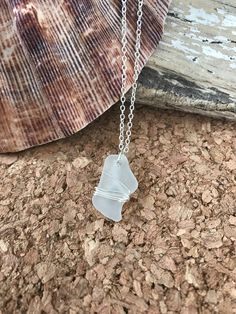 a white sea glass necklace on a chain next to a seashell and stone wall