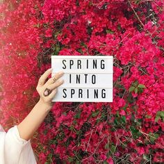 a woman holding up a sign that says spring into spring in front of pink flowers