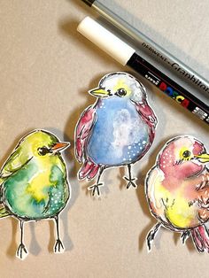 three watercolor birds sitting on top of a table next to a marker