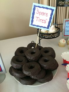 there are many chocolate donuts on the plate and cupcakes in the background