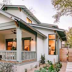 a white house with lots of windows and plants on the front porch, next to a wooden fence