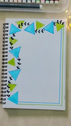 an open notebook with blue and green triangles on it next to markers, crayons, and pencils