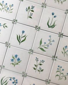 blue flowers and green leaves are painted on white tiles in this tile design that is part of a wall