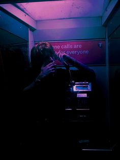 a person standing in front of a cell phone booth with a purple light on the ceiling