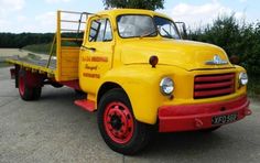 an old yellow truck parked on the side of the road with trees in the background