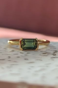 a green tourmaline ring sitting on top of a marble slab with a pink background