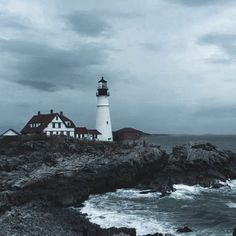 a lighthouse on top of a rocky outcropping next to the ocean under a cloudy sky