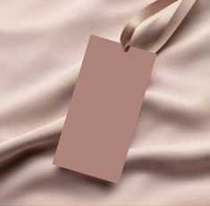 an empty tag is laying on a pink satin material with a beige ribbon around it