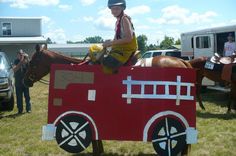 a young boy riding on the back of a horse in a fake firetruck