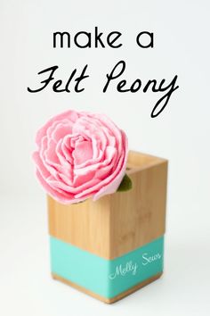 a pink flower sitting on top of a wooden block with the words make a felt peony