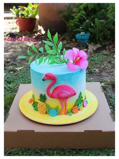 a cake decorated with a pink flamingo and pineapples on a cardboard box