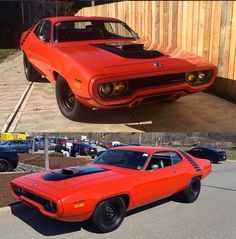 an orange muscle car parked in front of a wooden fence next to another red muscle car