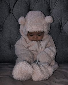 a baby dressed in a bear costume sitting on a bed with his eyes closed and hands folded