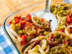 a glass casserole dish with onions, peppers, and meat in it on a blue towel