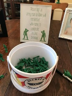 a bucket filled with green candies sitting on top of a wooden table next to a sign