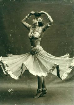 an old photo of a woman wearing a dress and hat with her hands behind her head