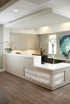 an empty reception area with wood flooring and white counter tops, flowers in vases on the wall