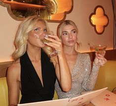 two women sitting at a table with drinks in their hands and papers on the table