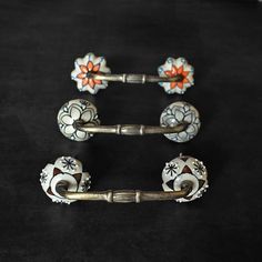 three decorative door handles with flowers on them, one is painted white and the other is orange