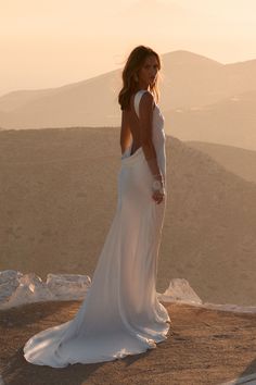 a woman in a white dress standing on top of a hill with her back to the camera