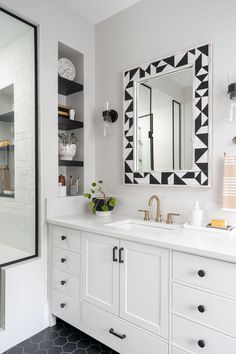 a white bathroom with black and white tile on the floor, mirror above the sink