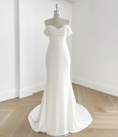 a white wedding dress on display in a room with wood flooring and wall behind it