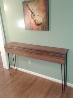 a long wooden table with hairpin legs in front of a painting on the wall