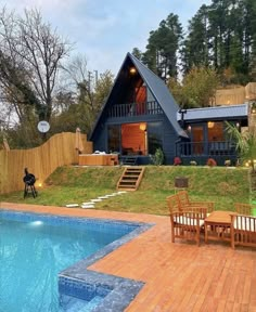 a house with a swimming pool in the yard and deck chairs around it, surrounded by trees