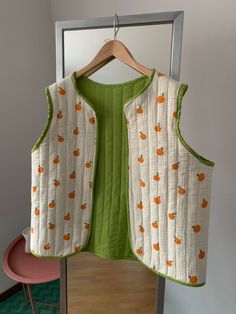 a white vest with oranges on it hanging from a hanger in front of a mirror