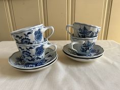 two blue and white cups and saucers sitting on a tablecloth with a wall in the background