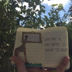 someone is holding an open book with writing on it and a giraffe in the background