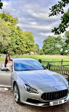 a woman sitting in the driver's seat of a silver sports car on gravel