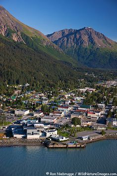 an aerial view of a town on the water with mountains in the backgroud