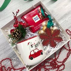 a christmas gift box with coffee mugs, candy and decorations on the table next to it