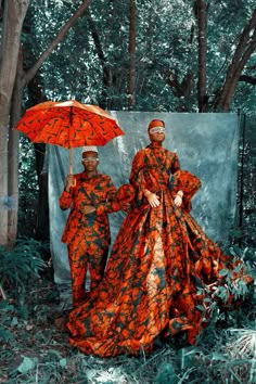 two people standing in the woods with an umbrella over their heads and wearing orange dresses