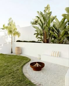 a white fenced in area with grass and plants next to it, along with a wooden bowl on the ground