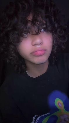 a close up of a person with curly hair wearing a black shirt and looking at the camera