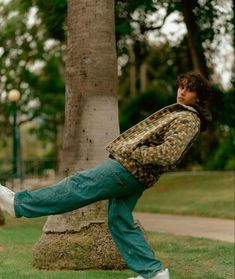 a young man is kicking a soccer ball in the park while leaning on a tree