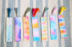 four colorful bookmarks with tassels are lined up on a striped cloth surface