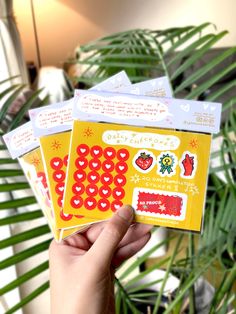 a person holding up three envelopes with stickers on them in front of a plant