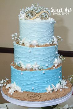 a three tiered blue and white cake with shells on it's bottom layer