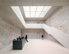 two people are walking in an empty room with exposed brick walls and skylights above