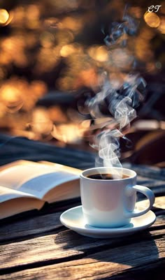 a cup of coffee sitting on top of a wooden table next to an open book